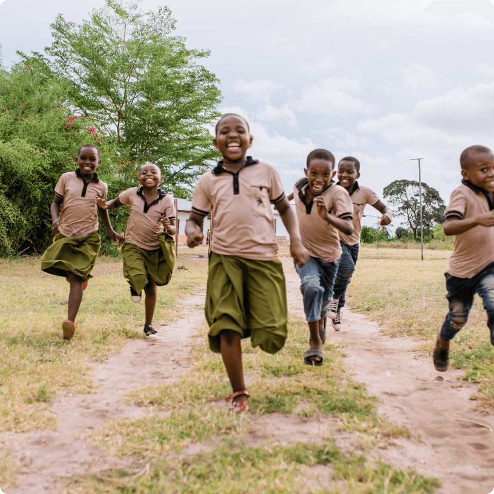 Six smiling children running in a field toward the camera.